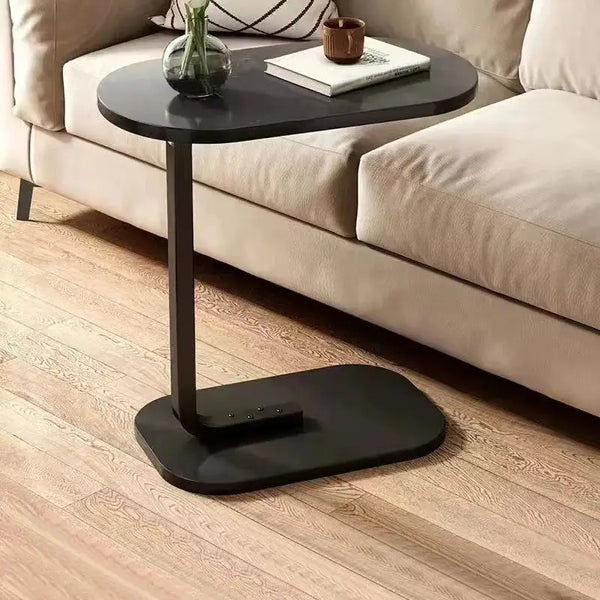 Minimalist black C-shaped side table positioned next to a sofa, featuring a sleek wooden top with a cup and book for convenience.