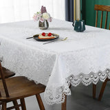 White floral lace tablecloth with scalloped edges on a wooden dining table. Waterproof and ideal for home, weddings, and special occasions.