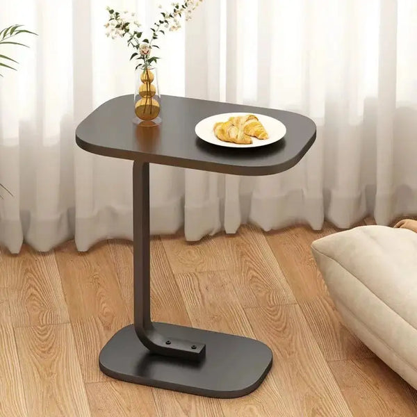 Modern C-shaped side table in black with a wooden top, placed beside a cozy seating area with a croissant and vase for decor.